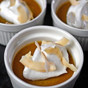 Close up photo of three paleo pumpkin custards topped with whipped coconut cream and toasted coconut flakes.