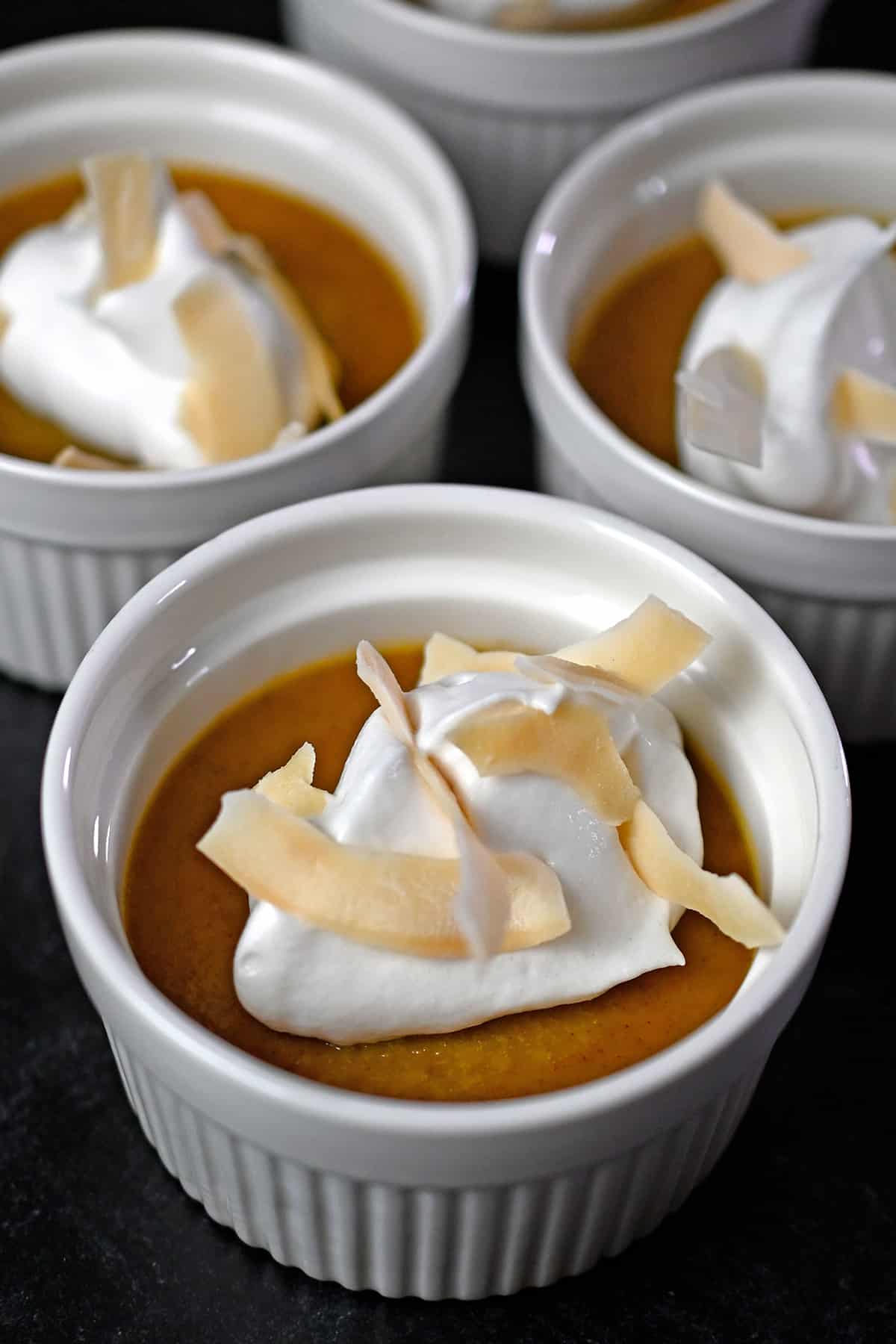 Close up photo of three paleo pumpkin custards topped with whipped coconut cream and toasted coconut flakes.