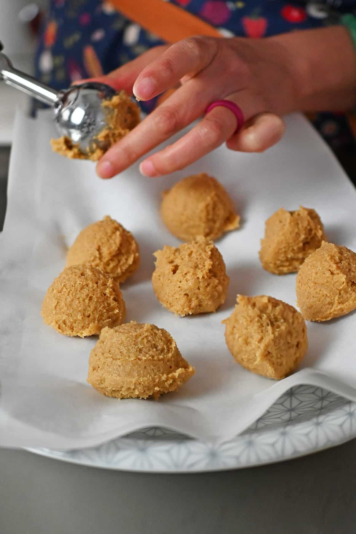 Raw snickerdoodle cookie dough balls being portioned out with an ice cream scoop on a parchment lined plate.