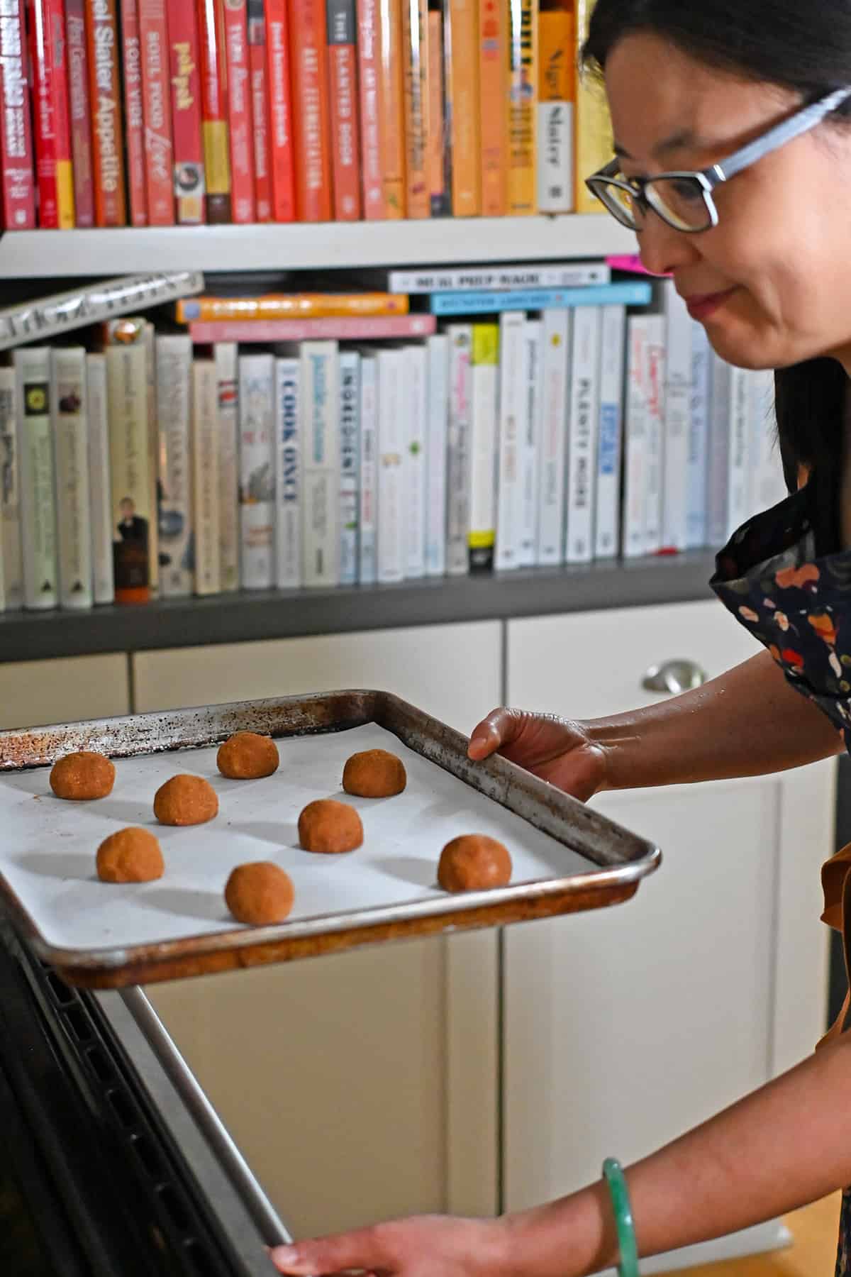 A smiling Asian woman putting a tray of paleo and gluten free snickerdoodles into the oven.