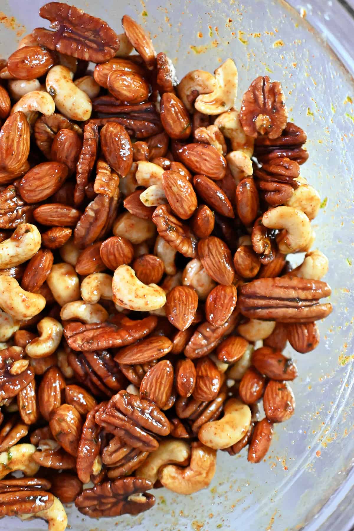Raw mixed nuts tossed in a spice-packed sauce in a large glass bowl.
