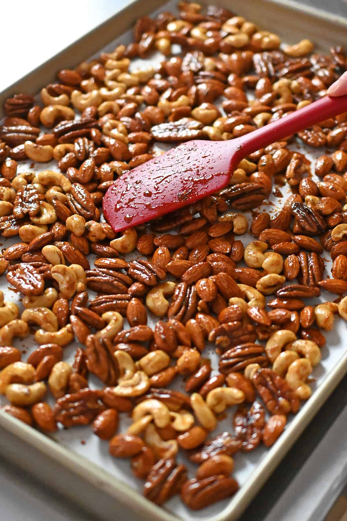 Using a silicone spatula to arrange the seasoned nuts in a single layer on a parchment lined rimmed baking sheet.