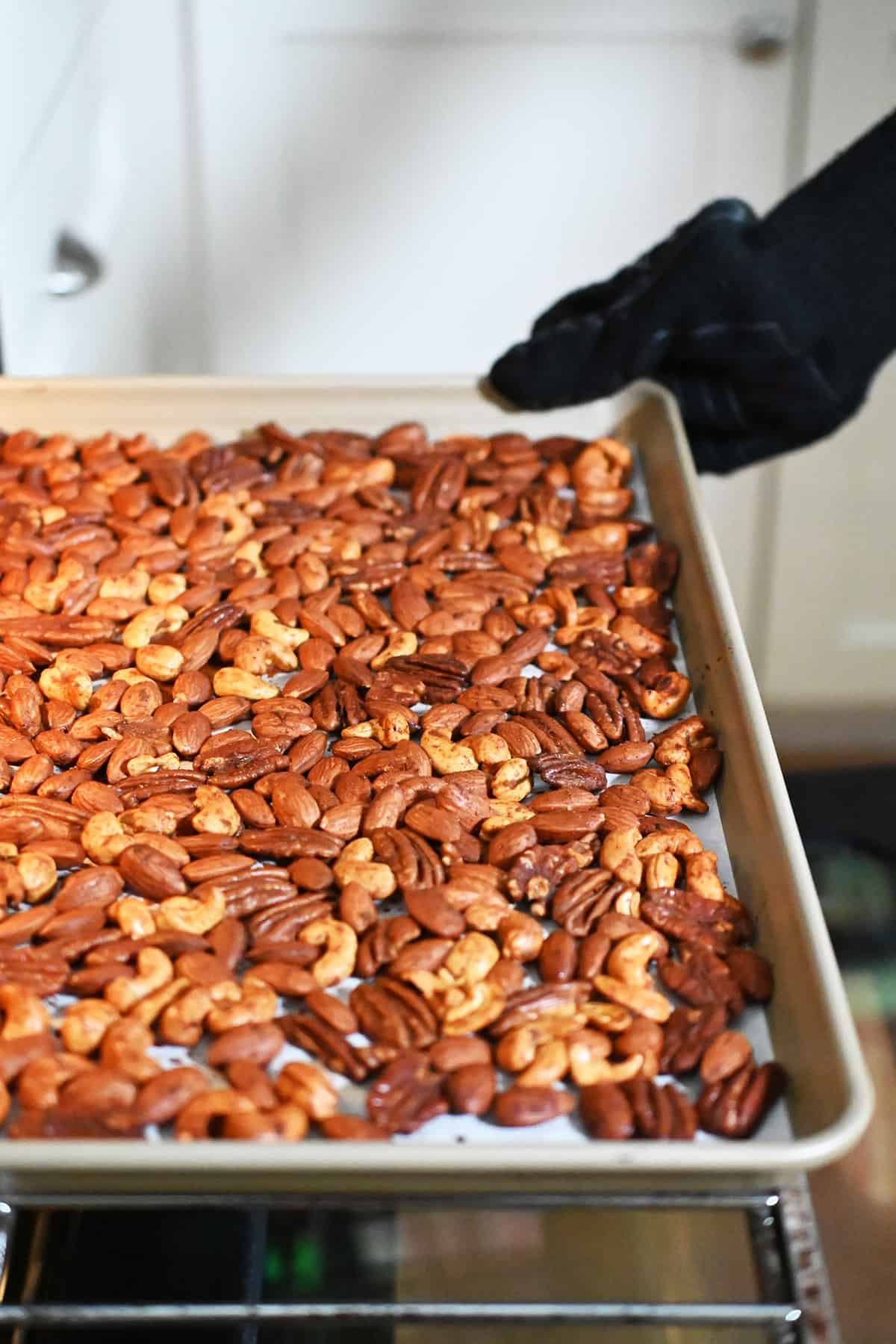 Removing a rimmed baking sheet of freshly roasted spice nuts out of an oven.