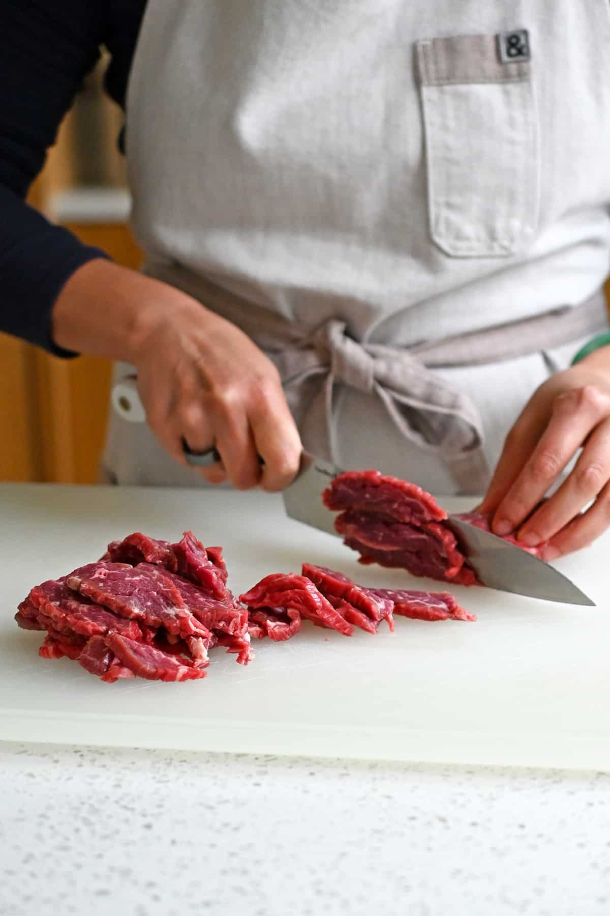 Slicing raw flank steak into thin strips against the grain with a chef's knife.