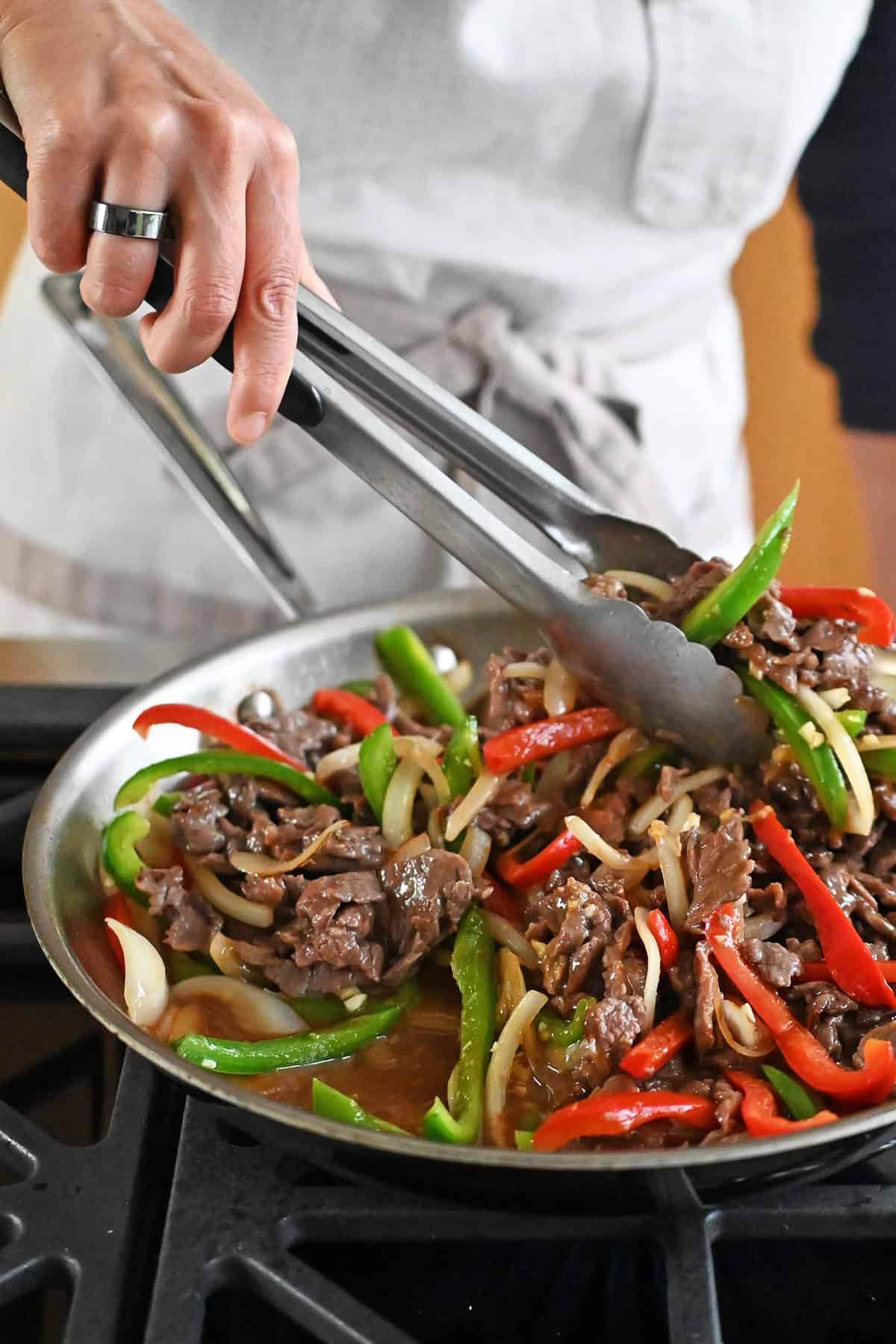 Tossing paleo and gluten free pepper steak in a skillet with a pair of tongs.