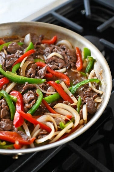 A side view of a skillet filled with cooked paleo and gluten free pepper steak.