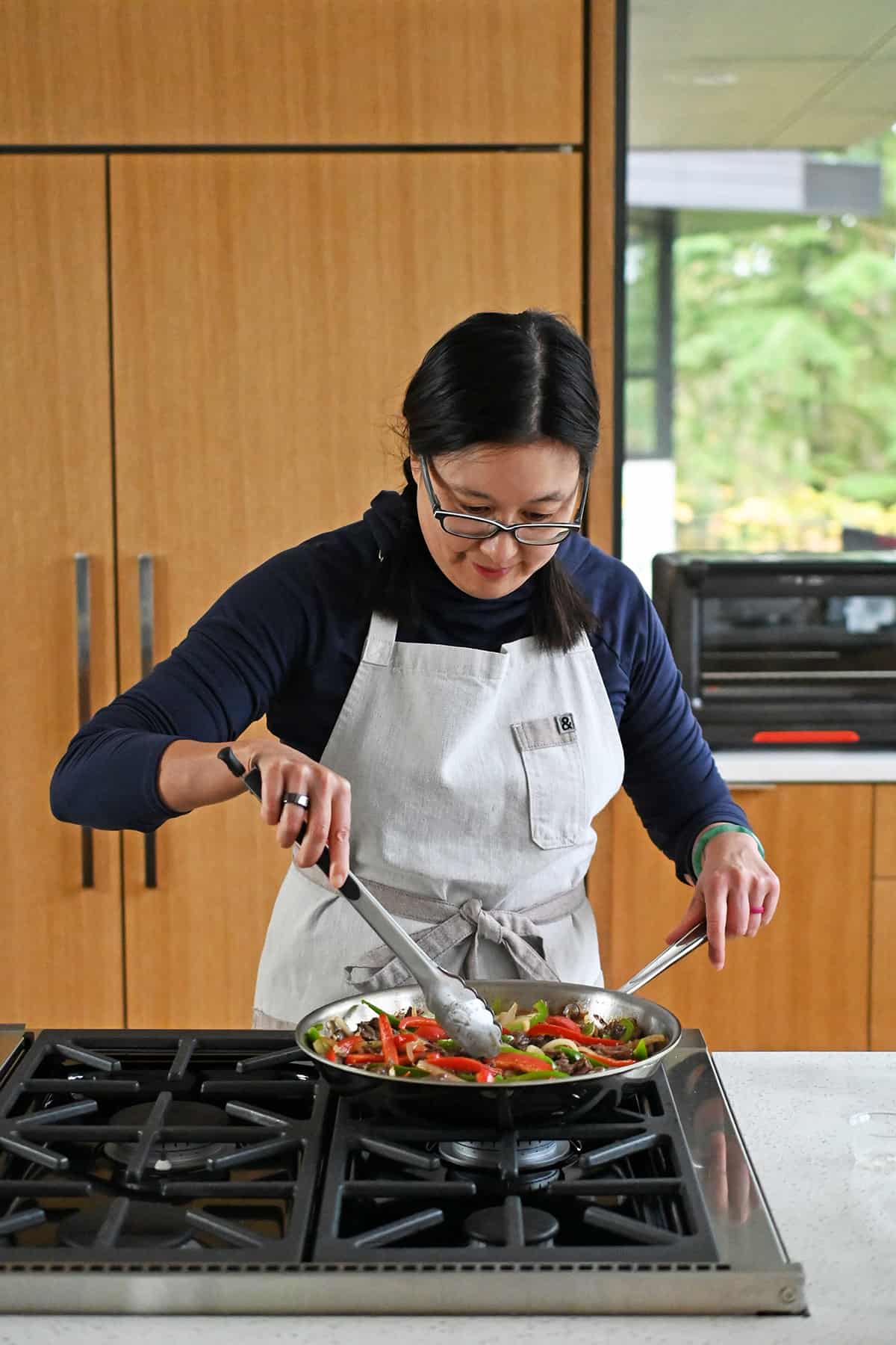 An Asian woman is cooking paleo and gluten free pepper steak in a skillet in a kitchen.