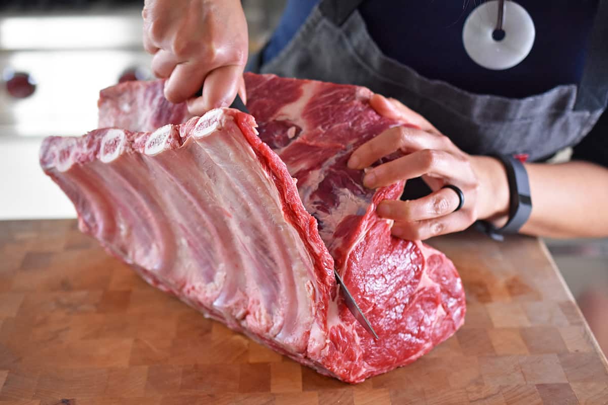 Someone using a boning knife to remove the bones from a raw prime rib roast.