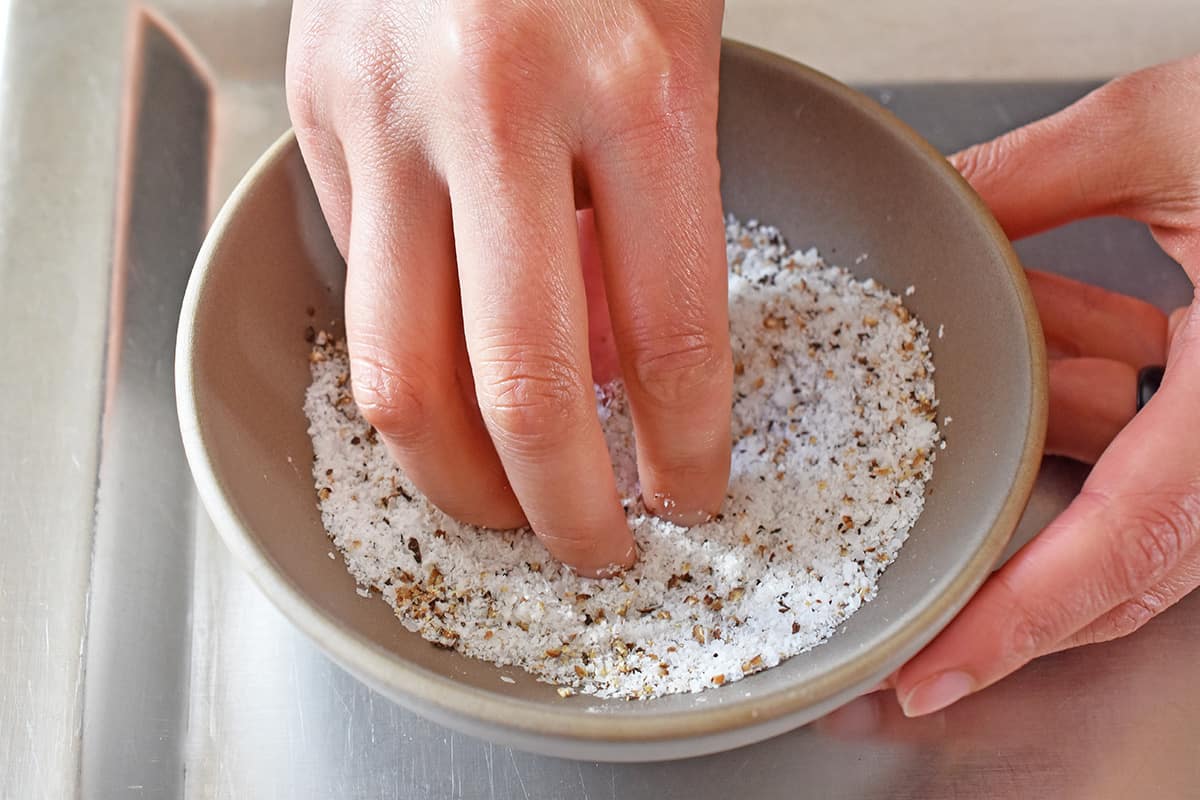 A hand is mixing some salt and pepper in a small bowl for the prime rib roast rub.