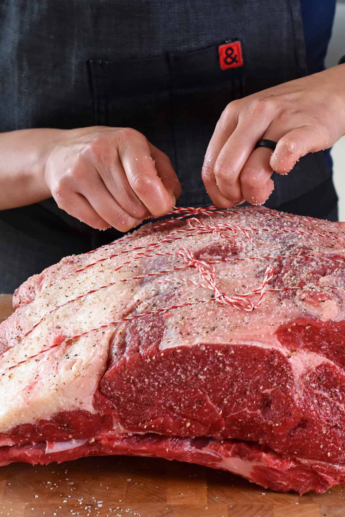 Tying a seasoned boneless prime rib roast onto the detached bone rack with butcher's twine.