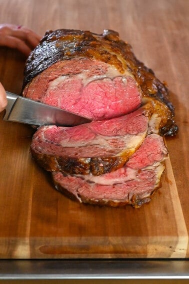 Someone slicing a medium rare prime rib roast on a wooden cutting board.