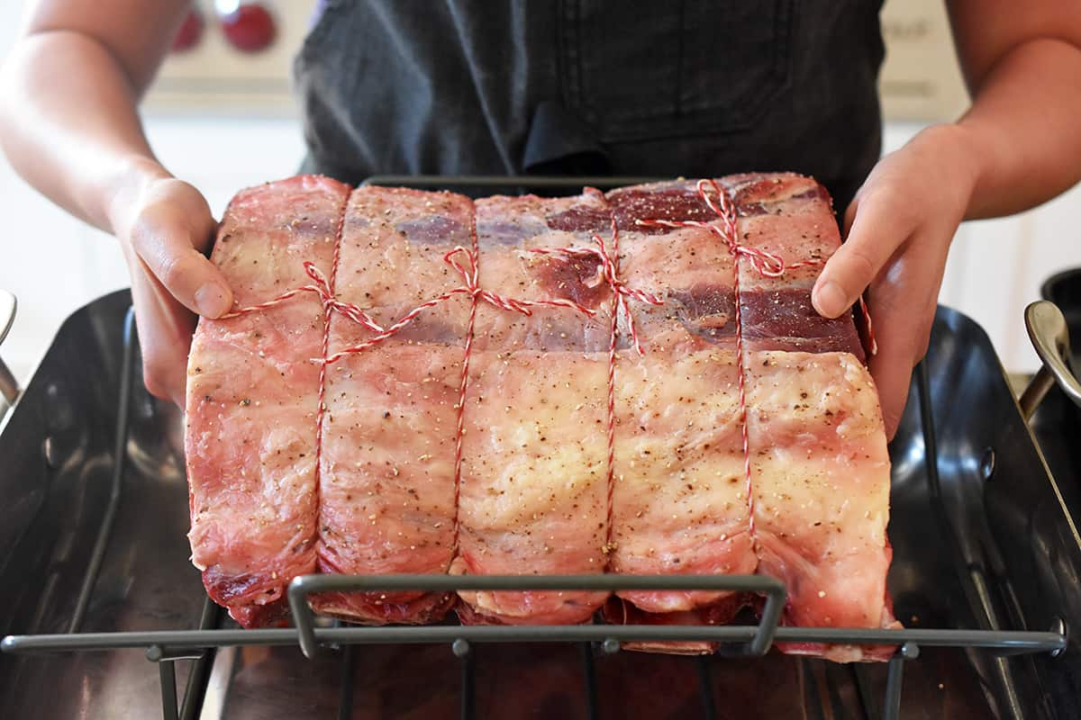 Placing a seasoned prime rib roast into a roasting rack in a roasting pan.