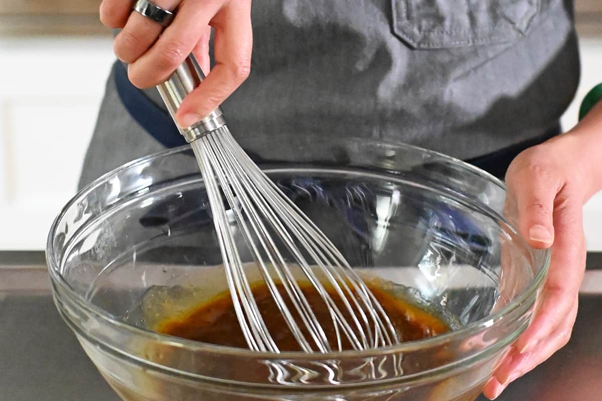 Using a metal whisk to combine the marinade ingredients in a large glass mixing bowl.