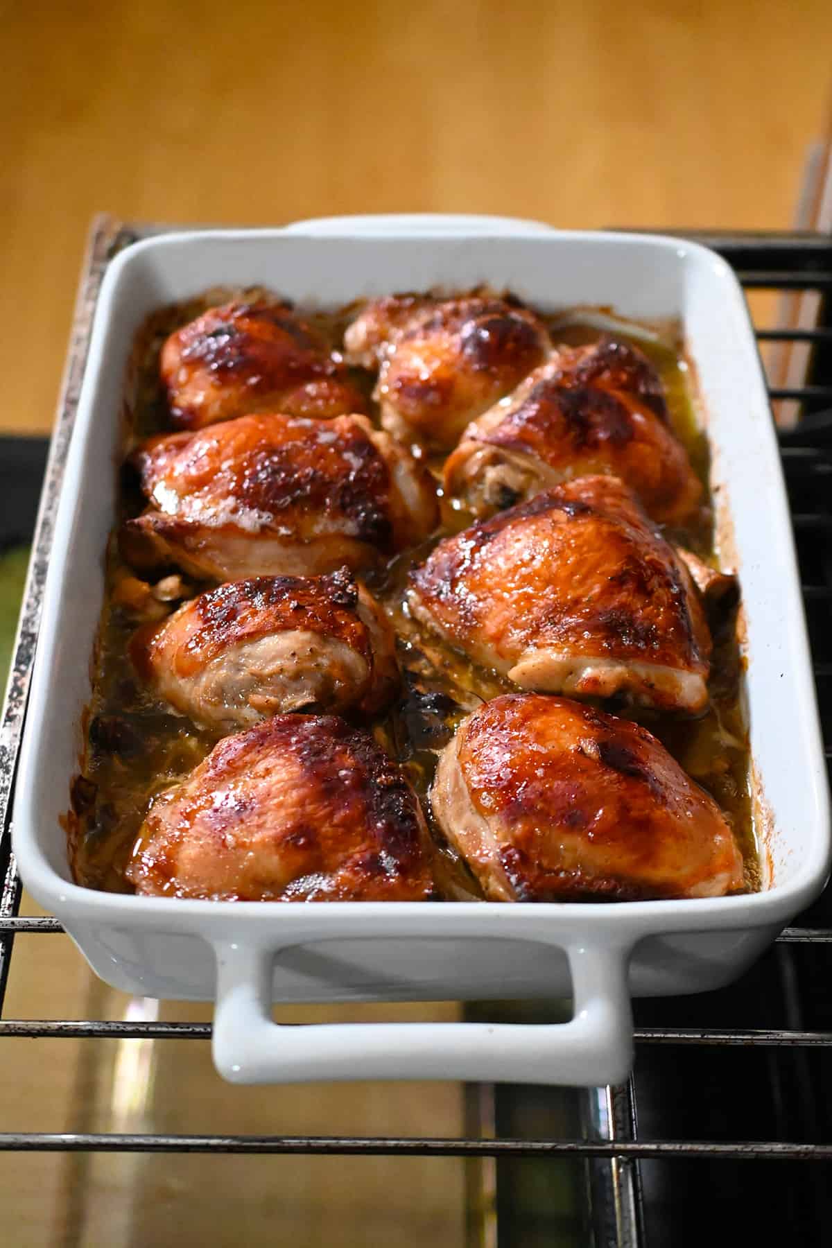 An open oven with a casserole dish filled with golden brown chicken thighs on top of tender roasted mushrooms.