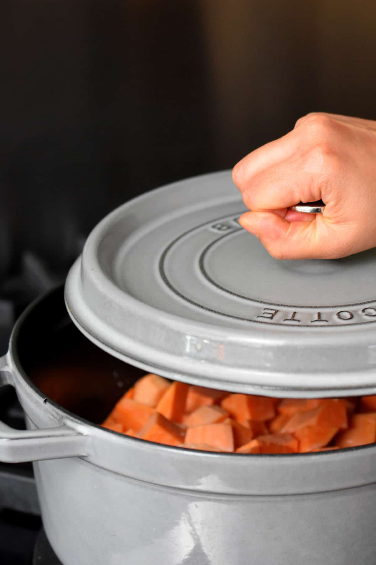 Placing a cover on a gray dutch oven filled with cubed sweet potatoes and coconut milk.