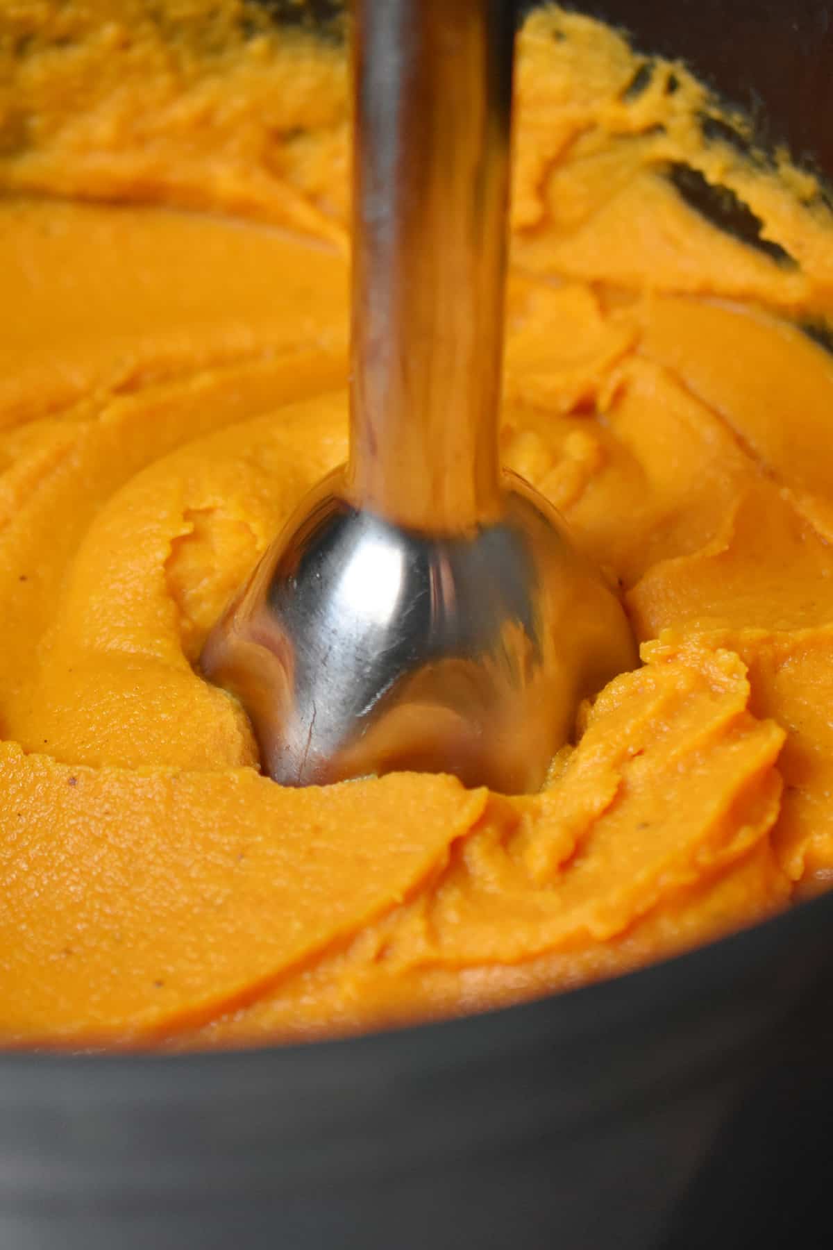 An immersion blender is blending cooked sweet potatoes and coconut milk into a silky puree.