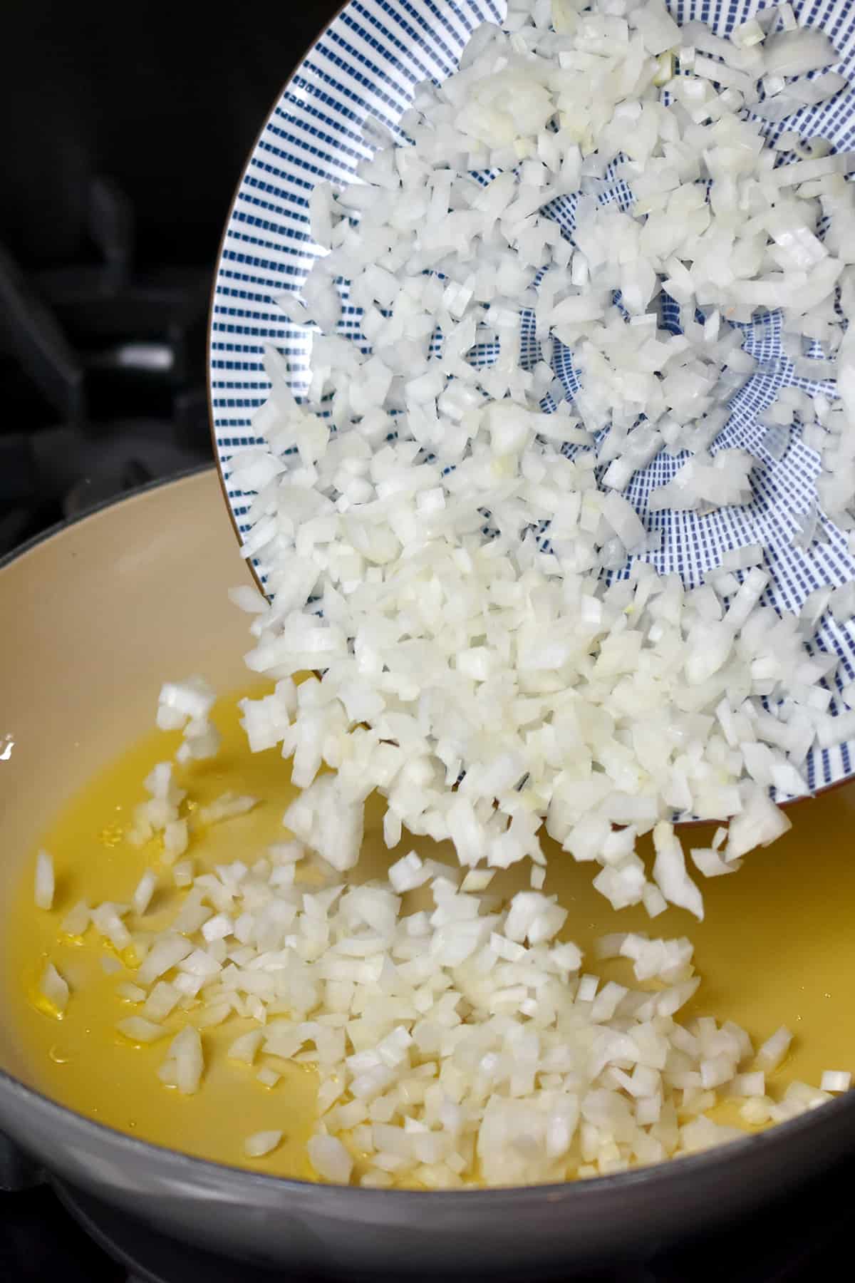 Adding chopping onions to a skillet filled with some hot oil.