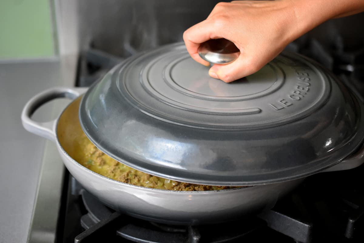Placing a lid on a enamel cast iron skillet filled with the Indian spiced shepherd's pie filling.