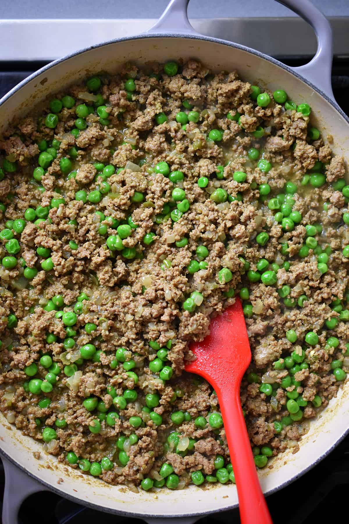 An overhead shot of a skillet filled with the Indian-spiced ground beef and green pea filling for an Indian-spiced shepherd's pie.