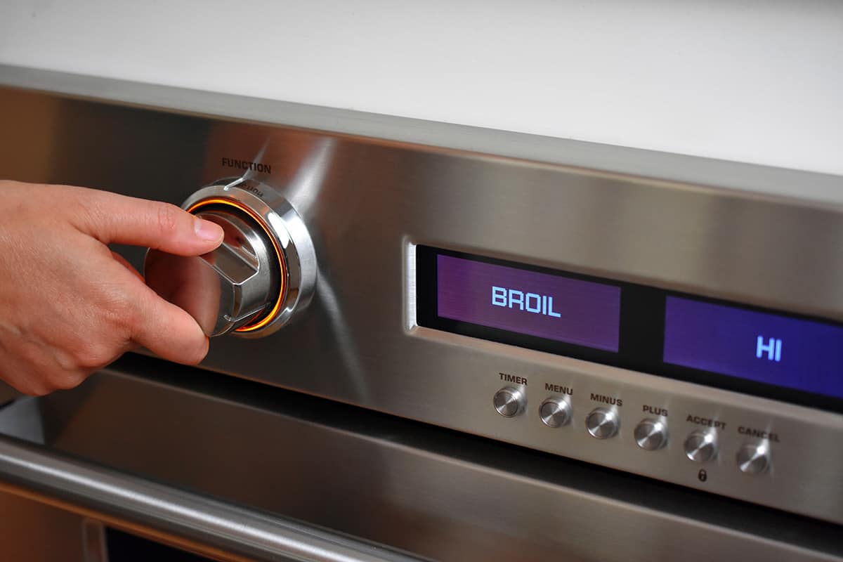 A hand is turning the knob on an oven to set it on broil.