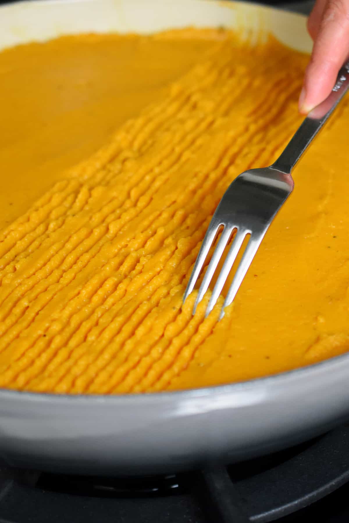 Using a fork to make a lines on top of the mashed sweet potato topping on an Indian-spiced shepherd's pie that is about to go under a broiler.