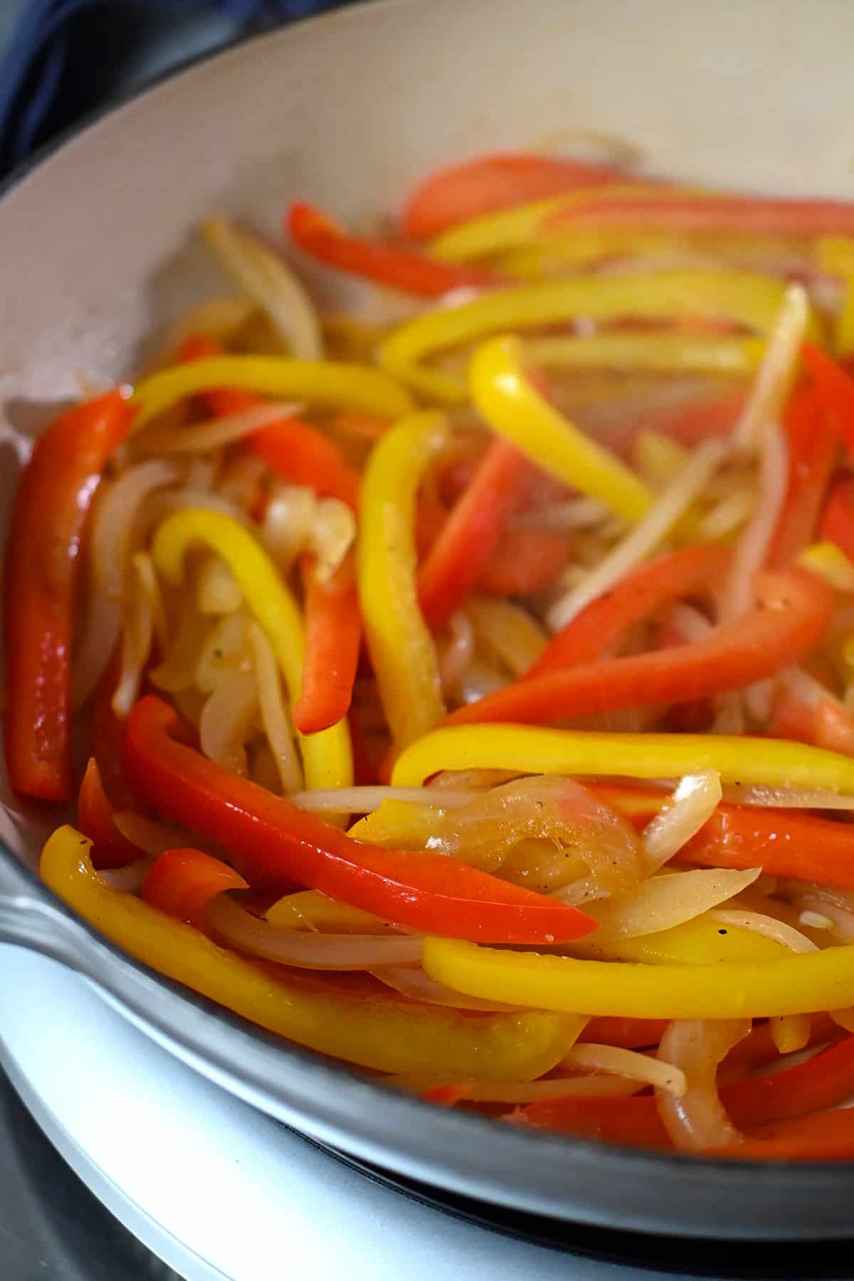 A closeup shot of an enamel cast iron skillet with sautéed thinly sliced bell peppers and onions for shrimp fajitas/