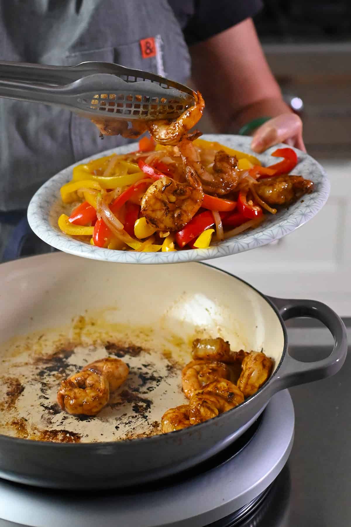 Transferring the cooked shrimp from the skillet to the plate with cooked fajita vegetables.