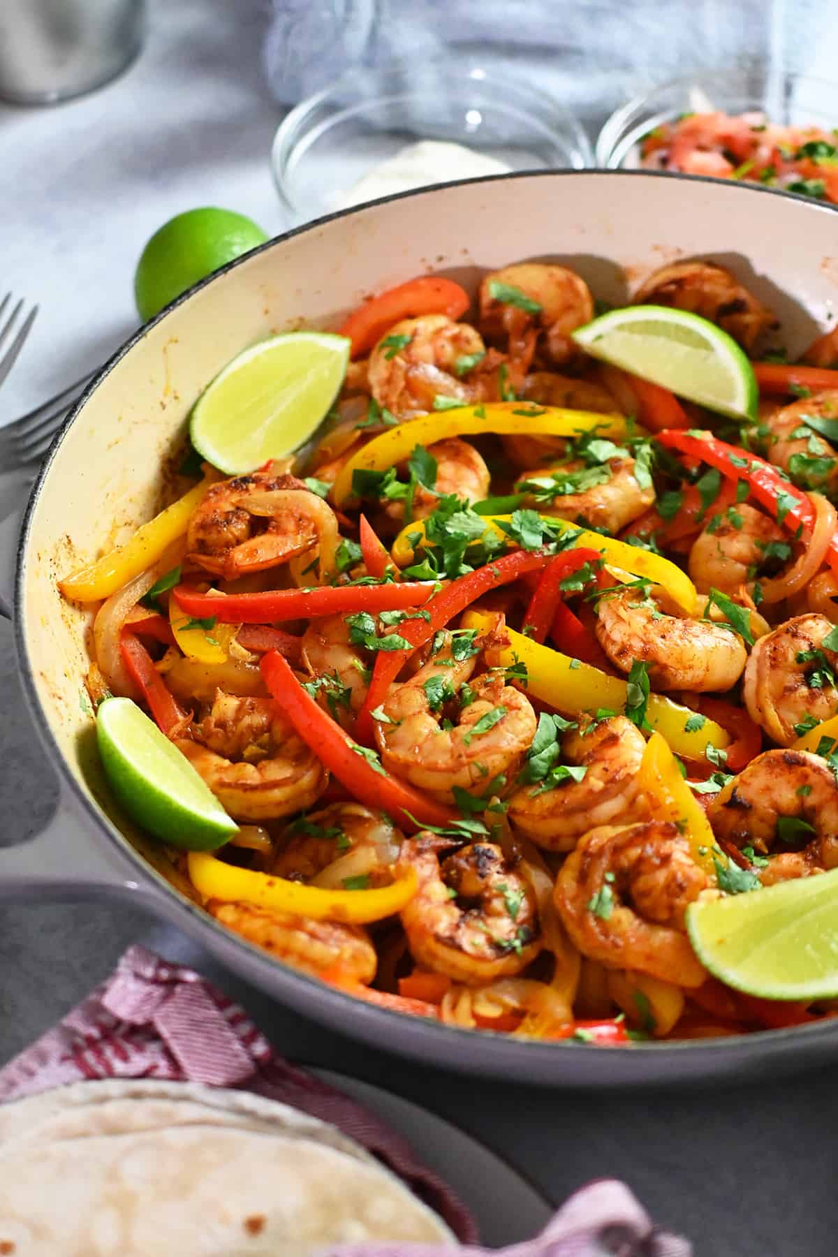A close-up side view of a skillet filled with shrimp fajitas and lime wedges.