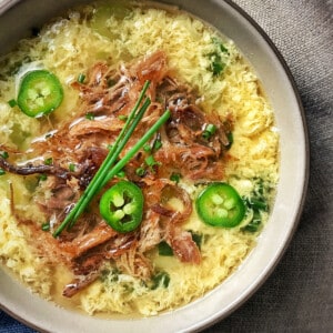 A bowl of egg drop soup topped with Kalua Pig, chives, and peppers.