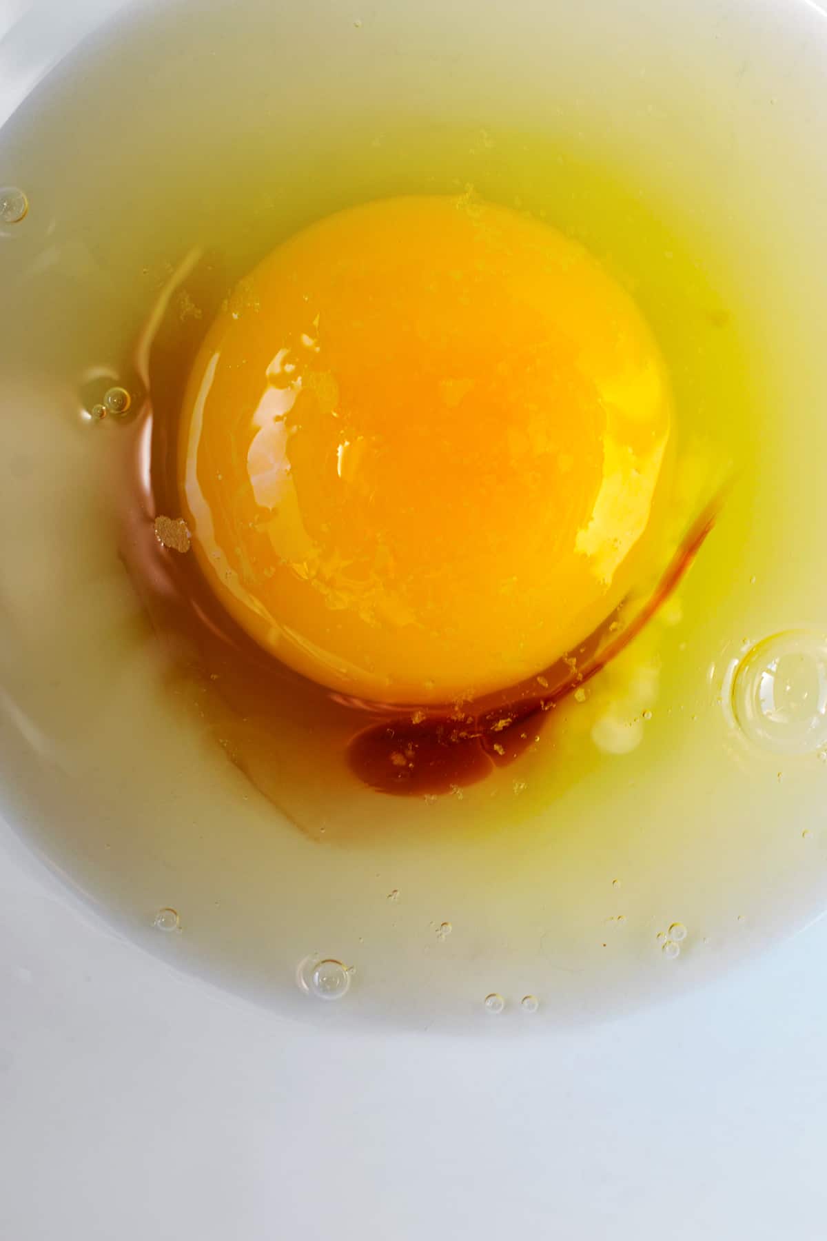 An overhead shot of a raw egg in a bowl with some fish sauce and salt.