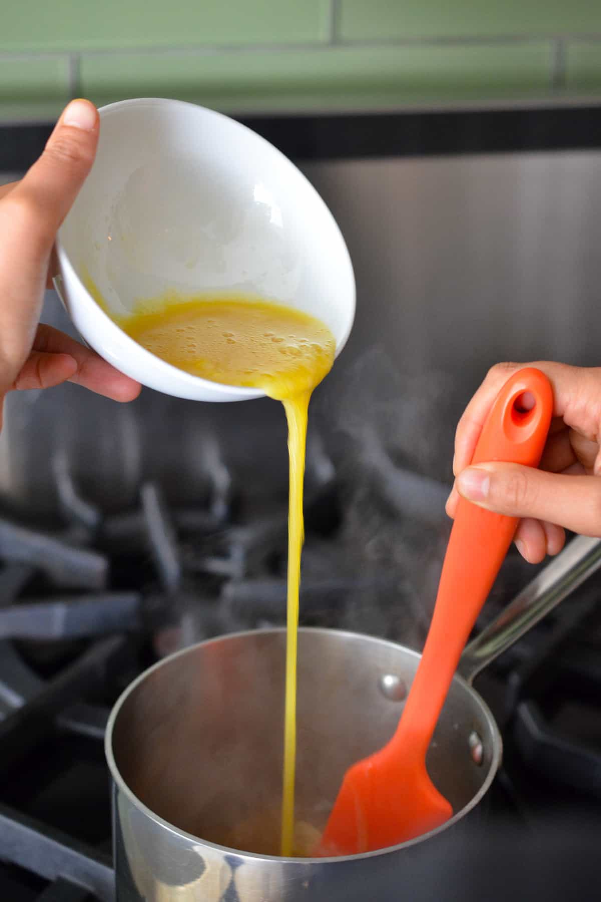 Pouring a raw whisked egg into a small saucepan with simmering broth.