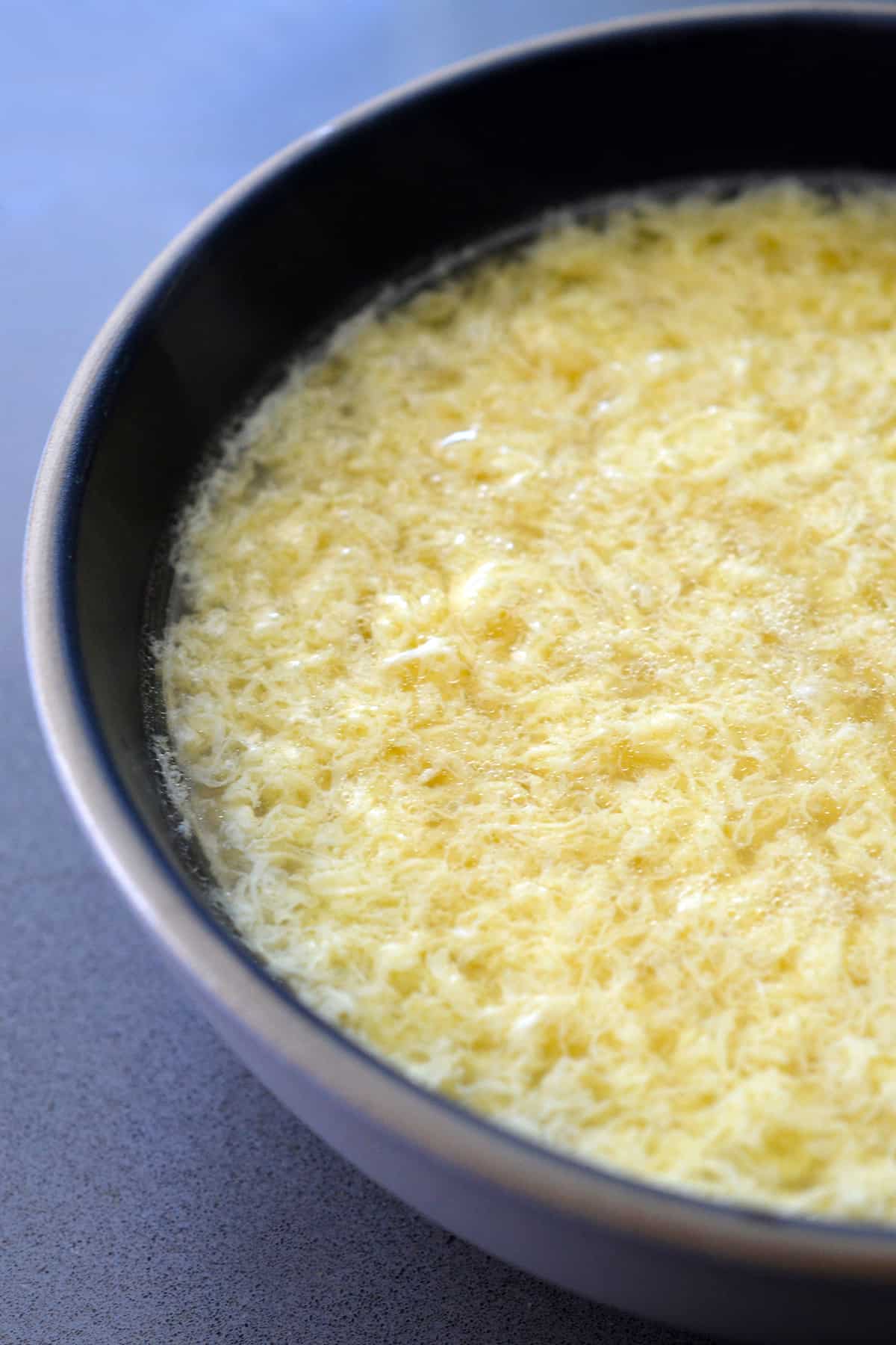 A side view of simple egg drop soup in a bowl with no garnishes.