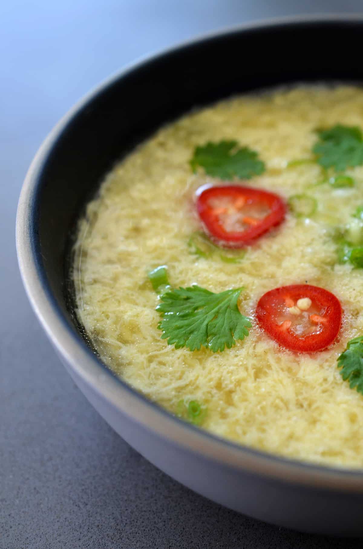 A bowl of egg drop soup topped with scallions, cilantro, and red peppers.