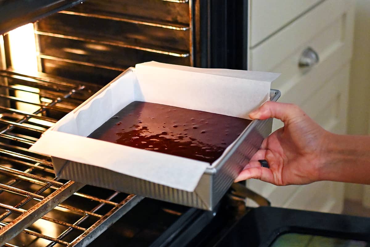 Placing a square pan of paleo brownie batter into an open oven.