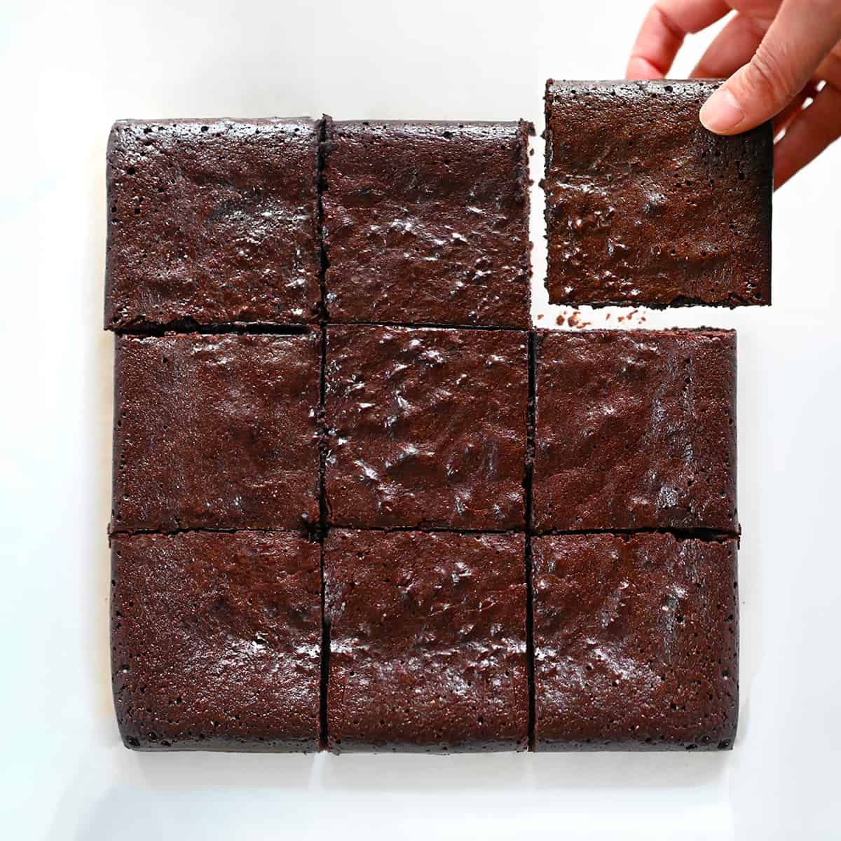 A hand is removing the corner square of a paleo brownie from a group of nine brownies.