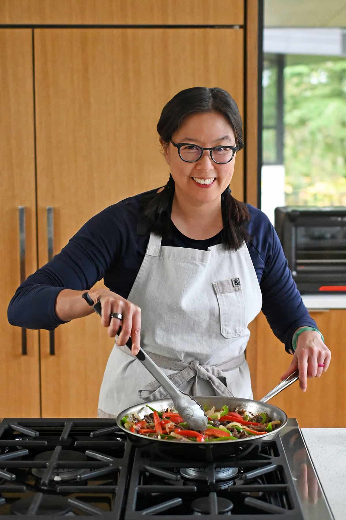 A photo of Michelle Tam of Nom Nom Paleo, an Asian woman in glasses, cooking a stir-fry on a range in a home kitchen