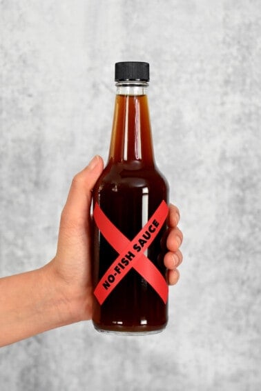 A hand is holding a bottle of homemade vegan fish sauce with a red label that says, "No-Fish Sauce"