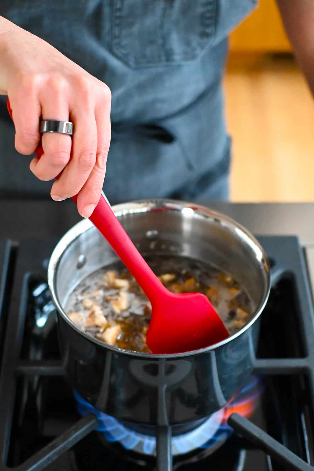 A red silicone spatula is used to stir the vegan fish sauce simmering in a small saucepan.