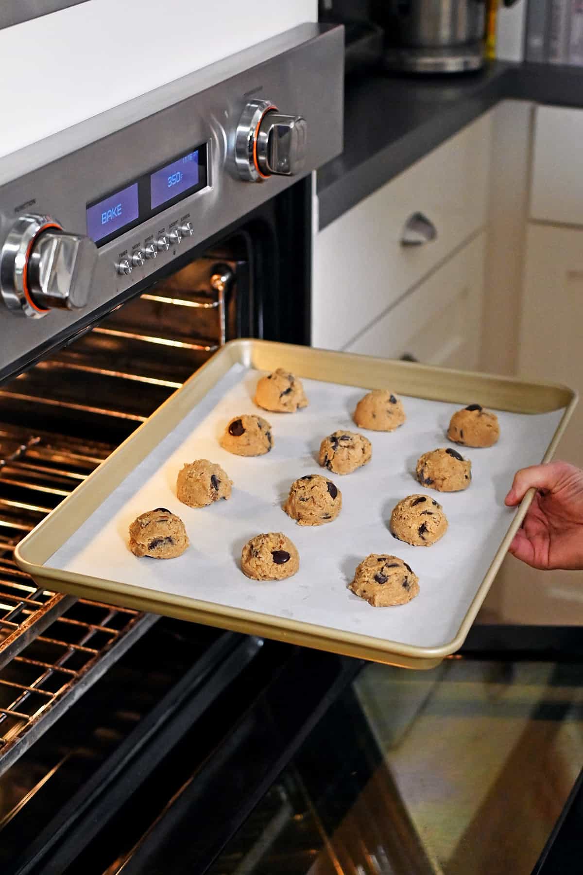 Placing a rimmed baking pan filled with banana cookie dough balls into an open oven to bake.