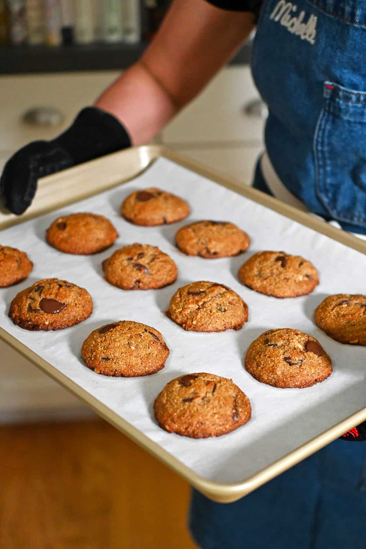 A person is holding a tray of freshly baked paleo banana chocolate chip cookies right out of the oven.