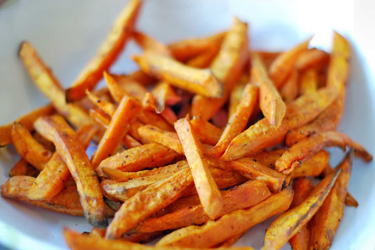 A closeup of a white bowl filled with sweet potato fries.