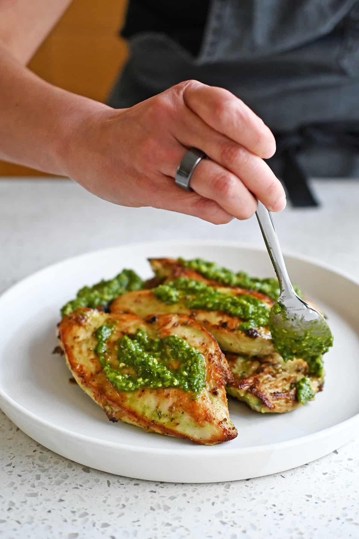 Spooning pesto onto a plate filled with pesto chicken cutlets right before serving.