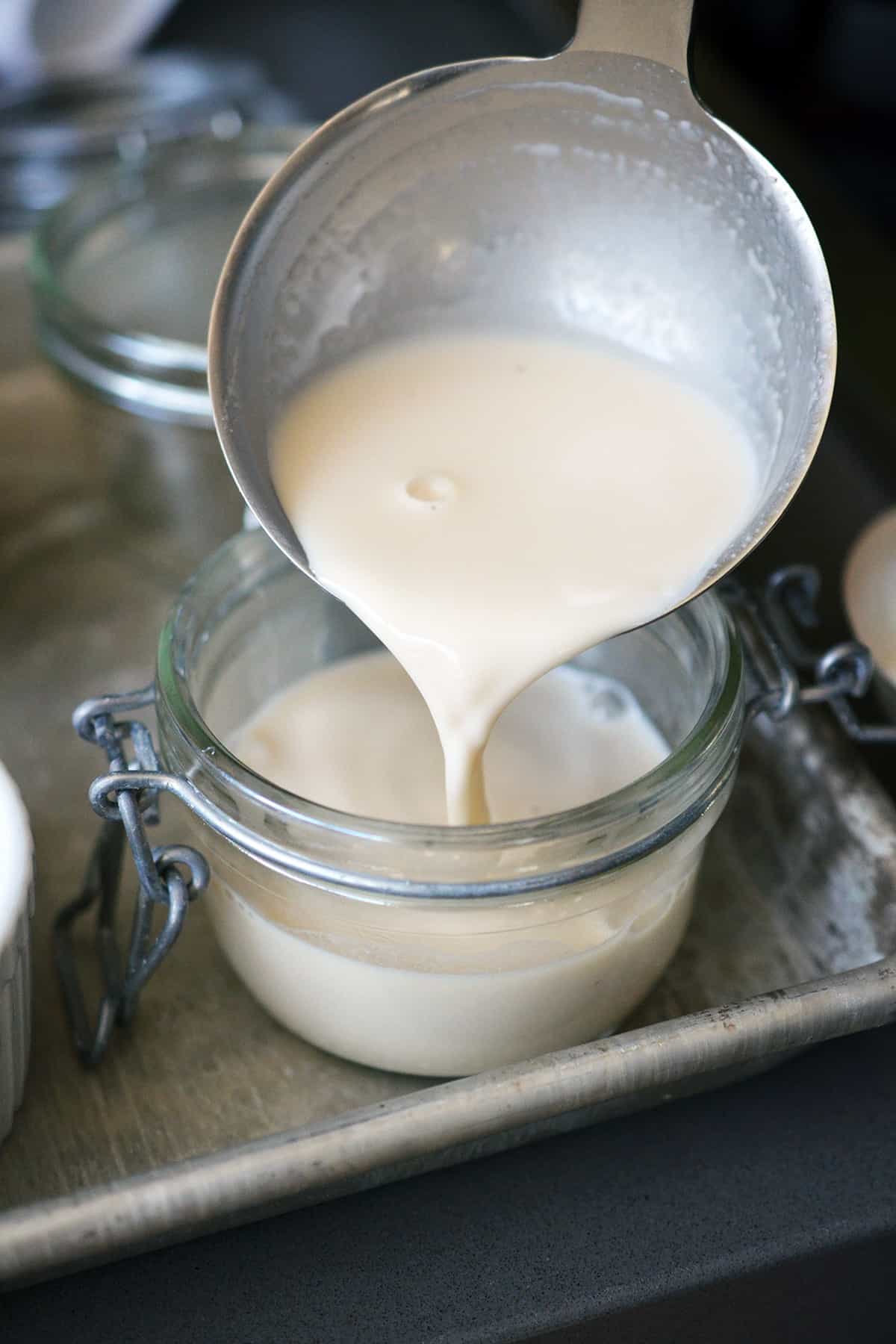 Ladling Panna Cotta into a glass jar with a lid before chilling it in the fridge.