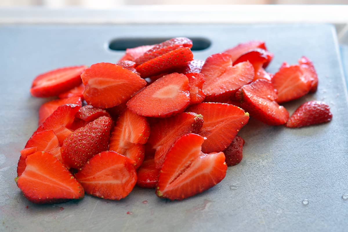 A pile of sliced strawberries on a gray cutting board.