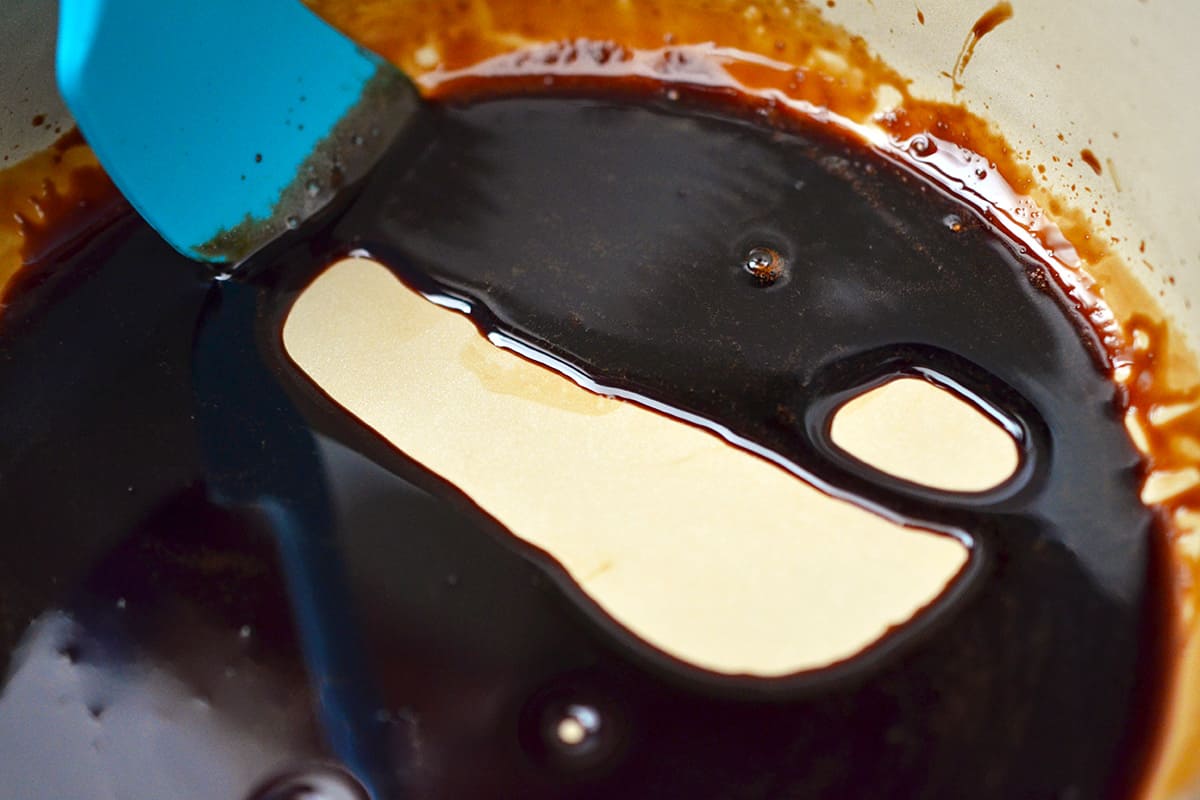 Reduced balsamic vinegar in a sauce pan where a blue silicone spatula shows how thick it is when dragged across the bottom of the pan.