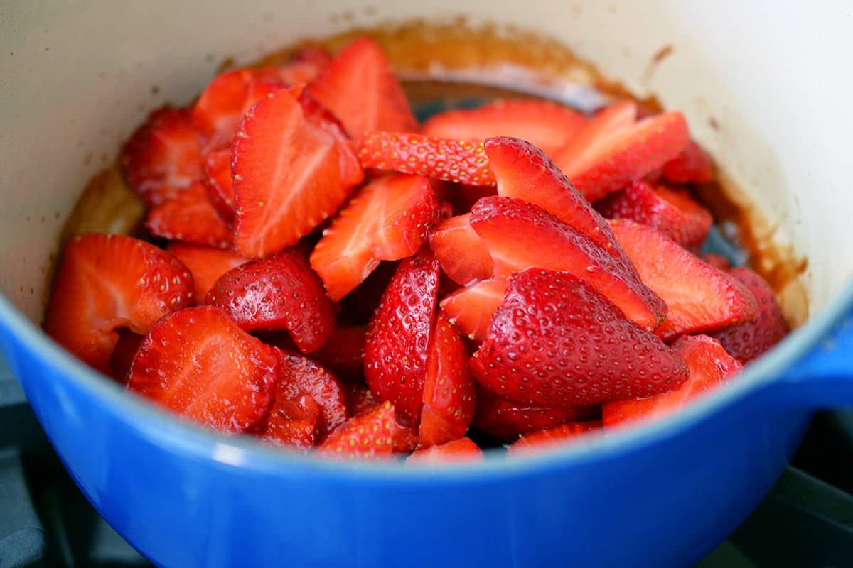 A closeup shot of sliced strawberries and balsamic vinegar in a blue saucepan.