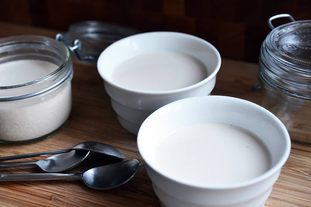 A side view of chilled Panna Cotta in white ramekins and in clear glass jars next to some teaspoons.