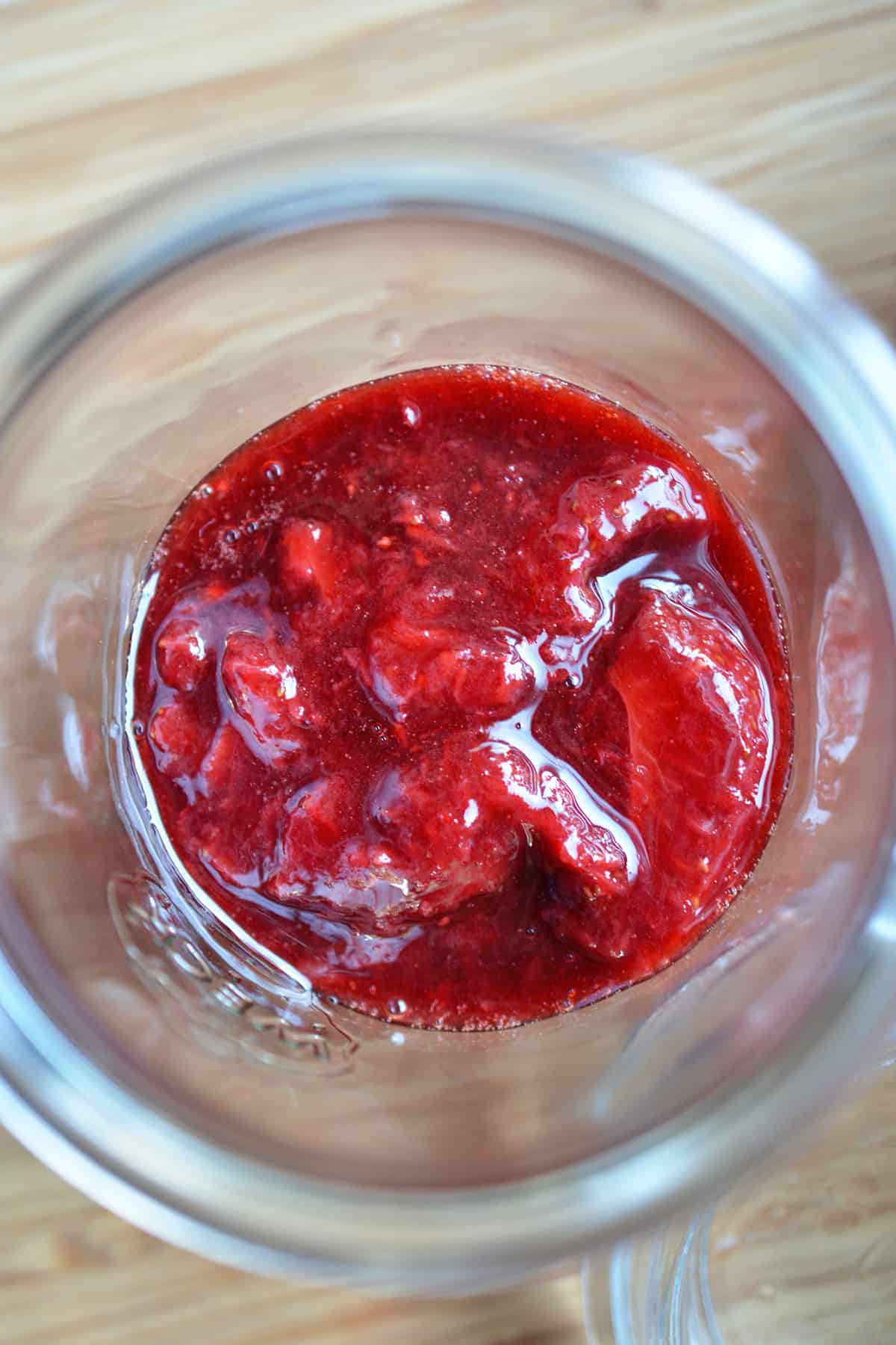 An overhead shot of a jar filled with strawberry balsamic compote, a topping for Panna Cotta.