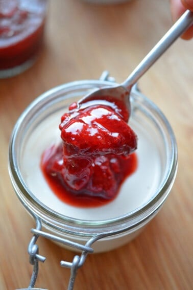 Adding a spoonful of strawberry compote to a jar filled with Panna Cotta.