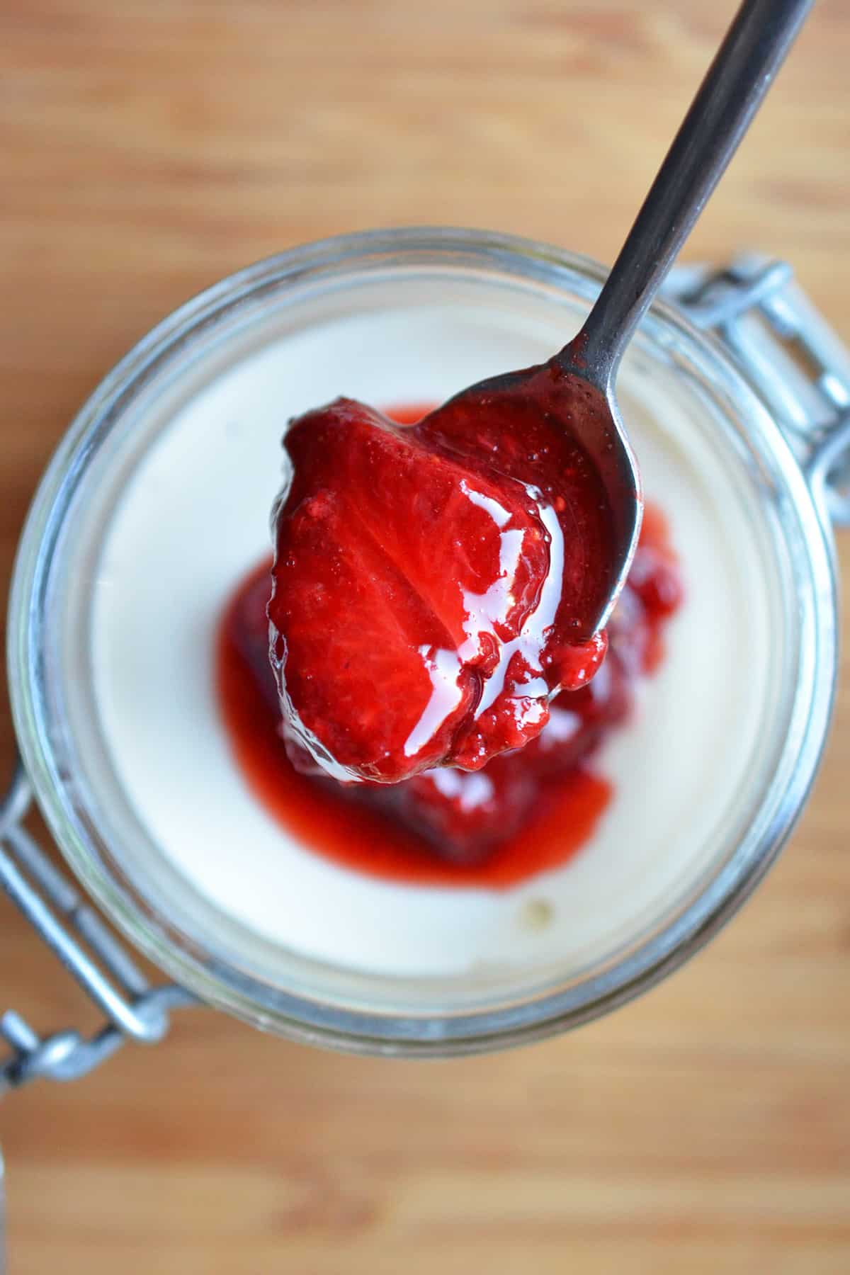 An overhead shot of strawberry Panna Cotta in a jar with a spoon lifting some up.